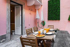 A breakfast table set with plates, glasses, and orange juice, with a green wall and a wooden table in the background. - Flores · Cozy Tailor Made With a Refreshing Terrace (Lisboa)
