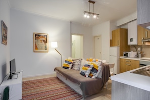 A compact living space with a sofa, a small desk, a kitchen area, and a dining table.