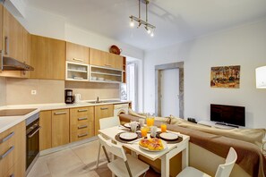 Een moderne keuken met houten kastjes, een eettafel gedekt voor twee personen en een televisie in de woonkamer.