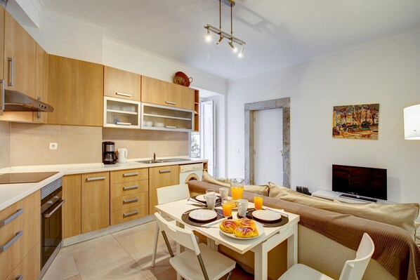 A modern kitchen with wooden cabinets, a dining table set for two, and a television in the living area.