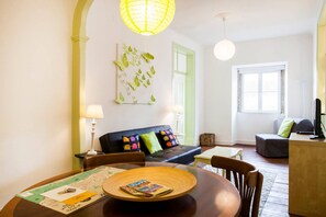 Un salon moderne avec une table à manger, un canapé agrémenté de coussins colorés, une grande fenêtre et une porte verte.
