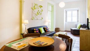 Un salón moderno con una mesa de comedor, un sofá con cojines de colores, un ventanal grande y una puerta verde.