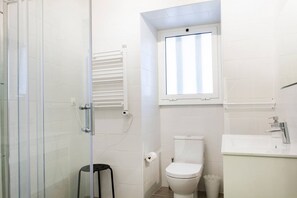 A bathroom with a glass shower enclosure, a white toilet, a sink with a mirror, and a window above the toilet.
