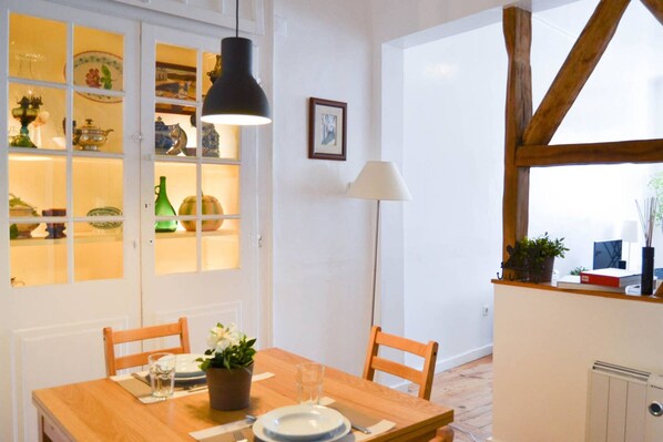A dining area with a wooden table, chairs, a potted plant, and a window with a view.