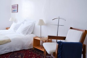 A hotel room with a bed, a chair, a nightstand, a lamp, and a wall-mounted shelf.