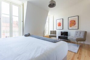 A modern bedroom with a large bed, a TV, a chair, and artwork on the wall.