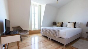 A bedroom with a bed, a desk with a computer, a chair, and a window.