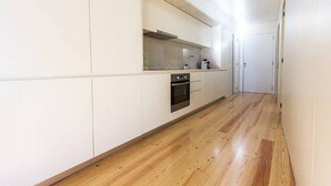 A narrow hallway with a kitchen area featuring white cabinets, a stainless steel oven, and a wooden floor.