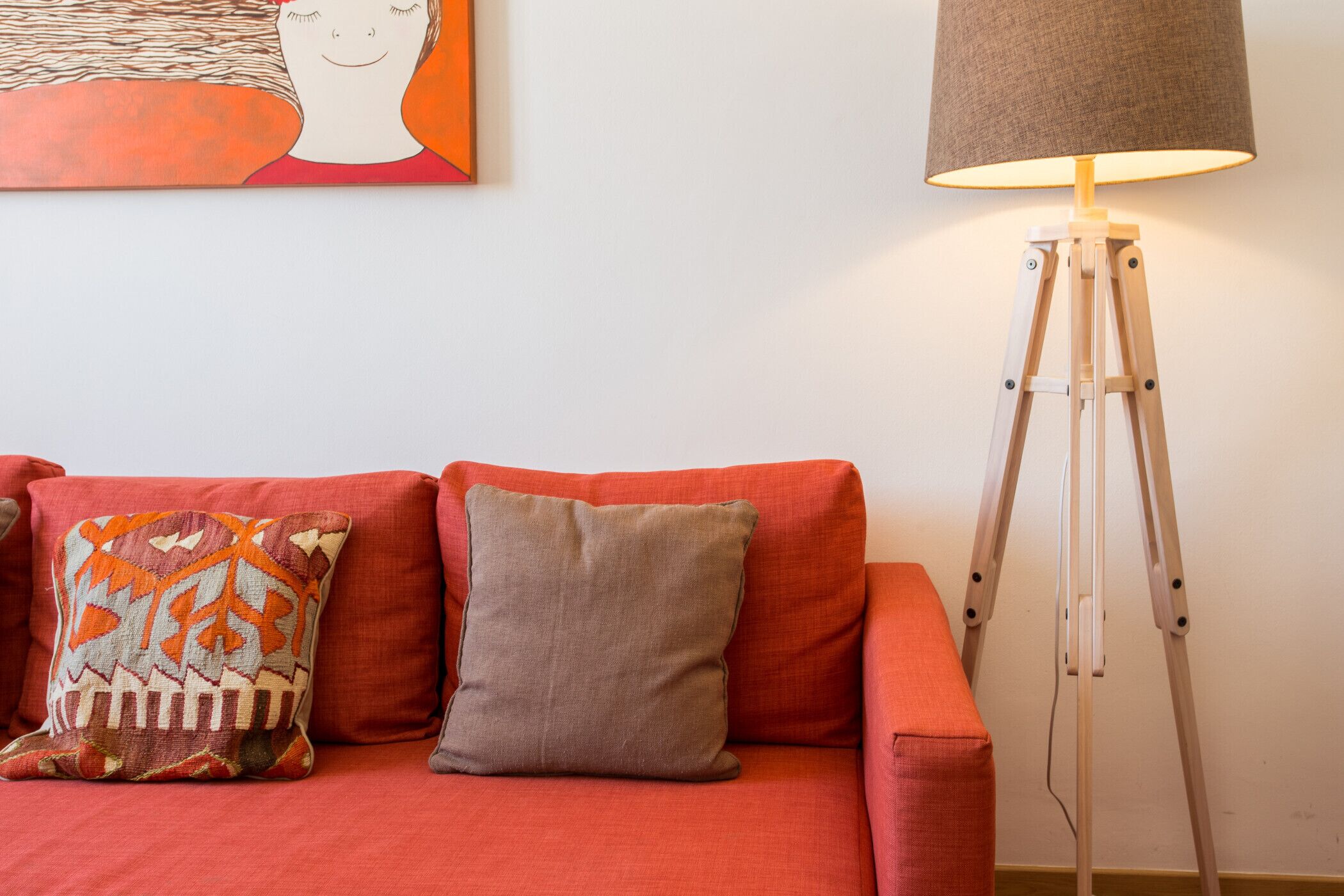 Um sofá vermelho com duas almofadas, um abajur e um quadro na parede.