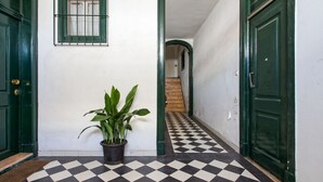 A hallway with a checkered floor, green doors, and a potted plant.