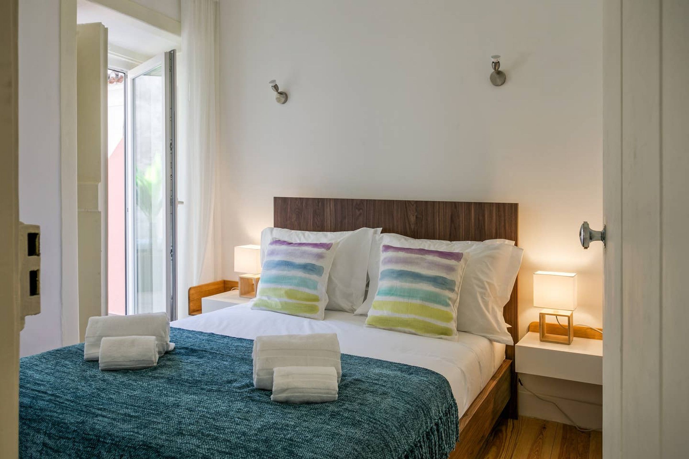 Ein ordentlich bezogenes Bett mit gestreifter Bettwäsche, einer türkisfarbenen Decke und zwei Nachttischlampen.