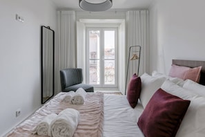 Un dormitorio con cama, una silla, un espejo y una ventana con vistas.