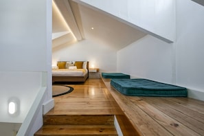 Un dormitorio con piso de madera, una cama con almohadas amarillas y un cojín verde.
