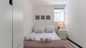 A small, modern bedroom with a bed, bedside tables, a lamp, and decorative tiles on the wall.
