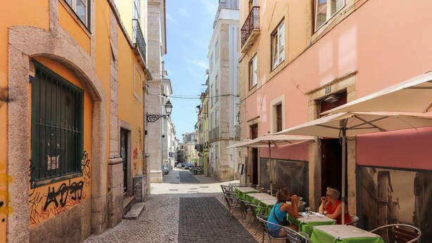 A narrow cobblestone street lined with buildings, outdoor seating with tables and chairs, and a few people dining.