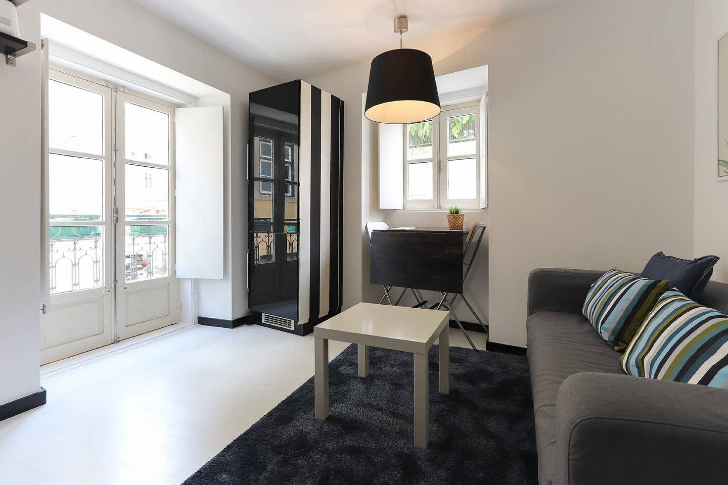 A modern living room with a grey sofa, a black and white striped pillow, a black floor lamp, and a white coffee table.