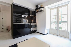 A modern kitchen with black cabinets, a microwave, and a stove. There is a window with a view of buildings outside. - Atalaia · Tailor Made Flat in Central Bairro Alto (Lisboa)