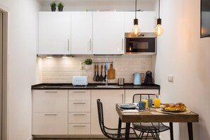 A compact kitchen with white cabinets, a black countertop, and a dining area with a table set for breakfast. - Metade · Charming Studio in Lisbon's Center (Lisboa)