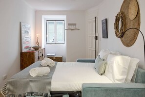 Quarto com cama, mesa de cabeceira, abajur e chapéu fixado na parede.