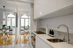 A modern kitchen with white cabinetry, a stainless steel sink, and a dining area with a glass table and chairs.