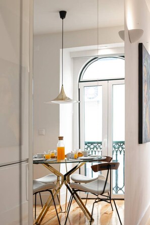 A modern kitchen with a glass dining table, two chairs, and a pendant light.