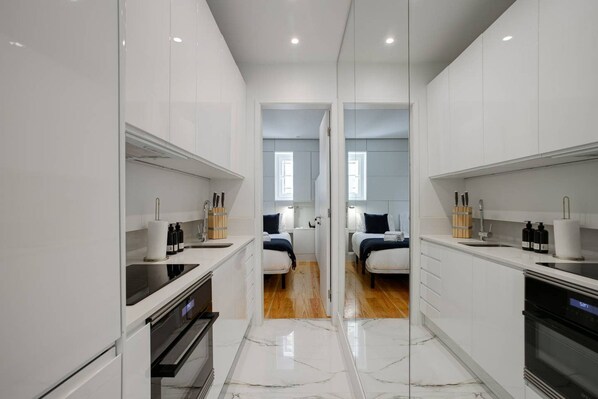A modern, compact kitchen with white cabinetry, a built-in oven, and a countertop with kitchen essentials.