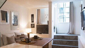Una sala de estar moderna con un sofá, una mesa de centro y obras de arte en las paredes. Se ve una escalera que lleva a un balcón con vistas.