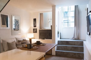 A modern living room with a sofa, coffee table, and artwork on the walls. There is a staircase leading to a balcony with a view.