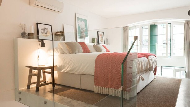 Un dormitorio con cama, mesita de noche, lámpara y una obra de arte en la pared.
