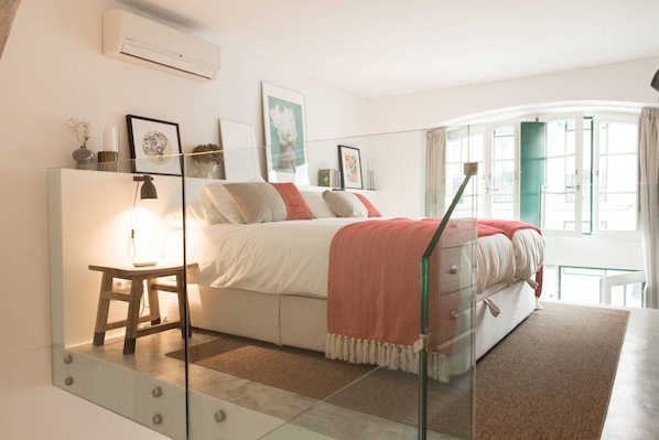 Un dormitorio con cama, mesita de noche, lámpara y una obra de arte en la pared.