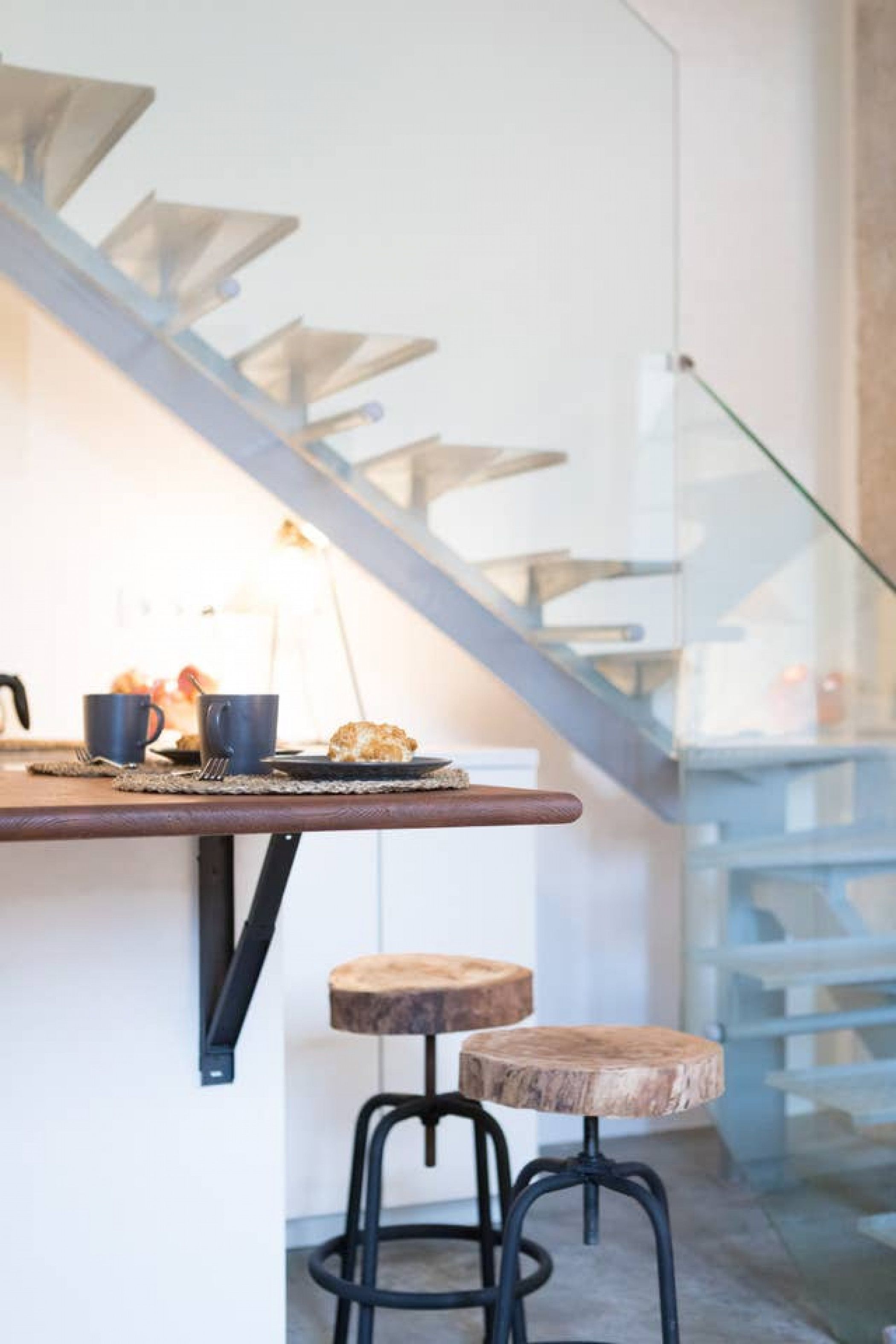 A modern kitchen with a wooden countertop, two stools, and a staircase.