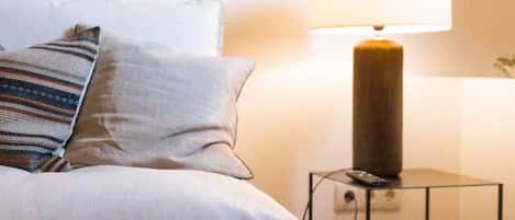 Ein ordentlich bezogenes Bett mit Kissen, einer Nachttischlampe und einem gerahmten Bild an der Wand.