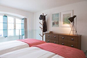 Een slaapkamer met een bed, een dressoir, een kapstok en een raam met gordijnen.