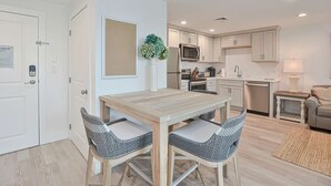 A modern kitchen with white cabinets, a microwave, and a dishwasher. There is a dining table with two chairs and a potted plant. - Premier Ocean View Corner Condo (875S.F.) (Plymouth)