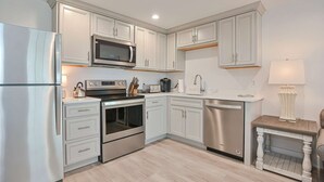 A modern kitchen with white cabinetry, stainless steel appliances, and a wooden table with a lamp. - Premier Ocean View Corner Condo (875S.F.) (Plymouth)
