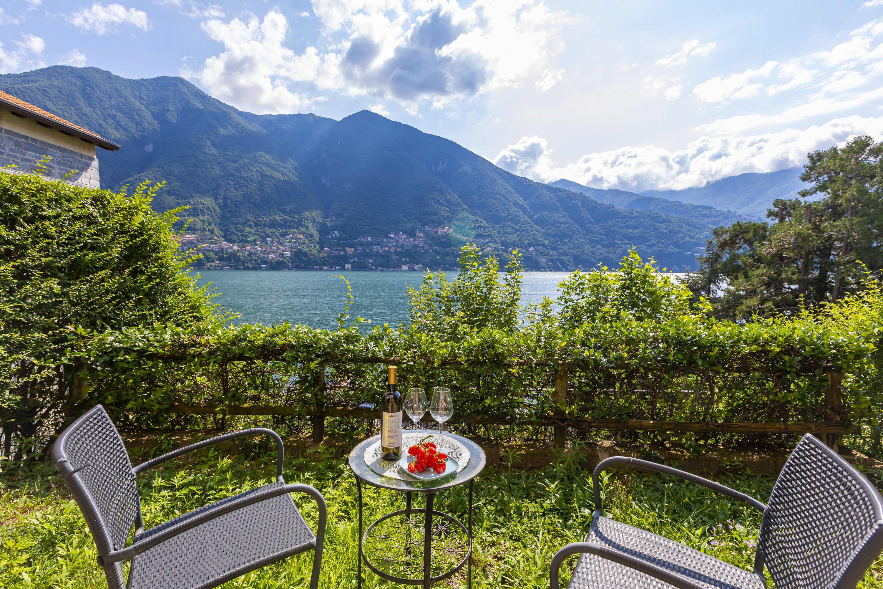 A terrace with two chairs and a table, overlooking a lake and mountains.