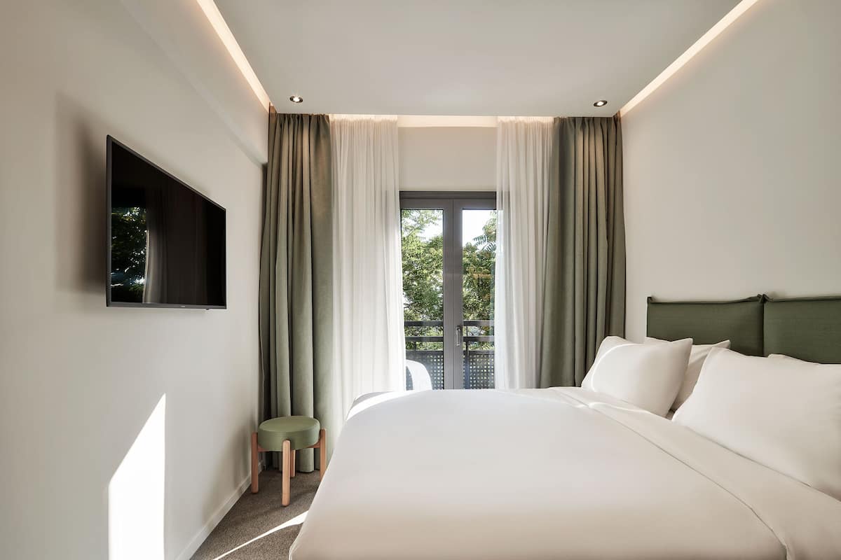 Una moderna camera d'albergo con un letto grande, una TV a schermo piatto fissata al muro e un balcone con tende.