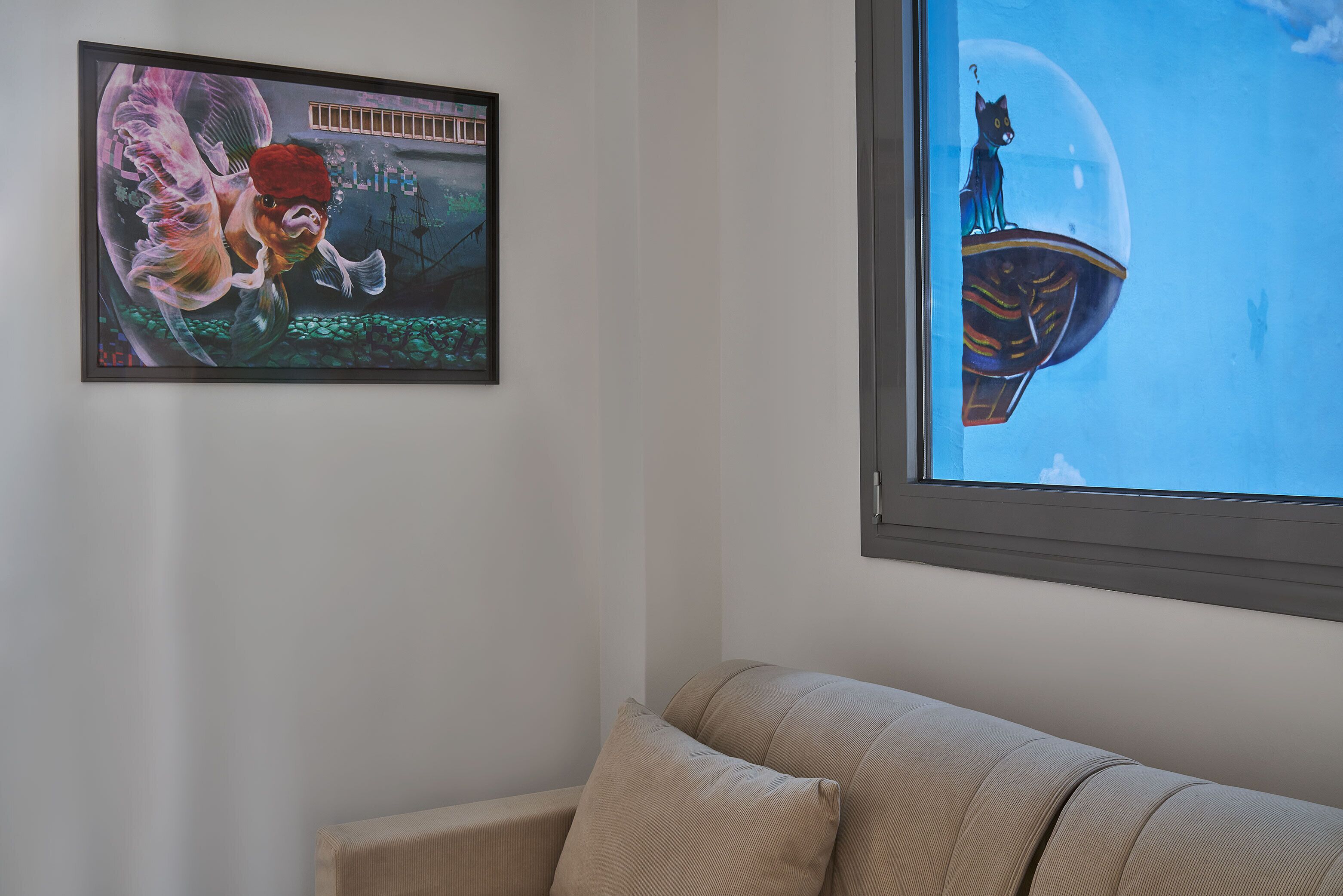 A room with a large window, a framed artwork on the wall, and a beige sofa.