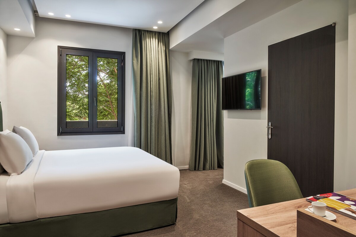 Habitació d'hotel amb llit, escriptori, cadira, televisió i finestra amb cortines.
