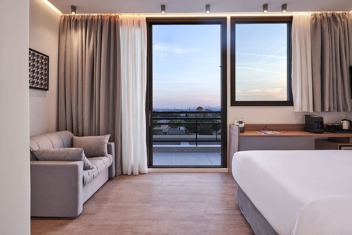 Una moderna camera d'albergo con un letto grande, un divano e un balcone con vista sulla città.