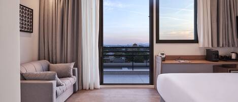 A modern hotel room with a large bed, a sofa, and a balcony with a city view.