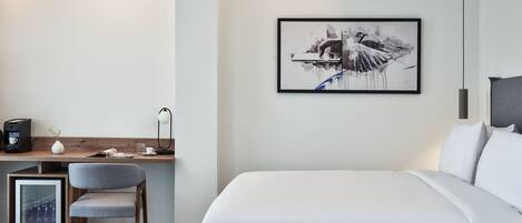 Une chambre d’hôtel moderne avec un lit soigneusement fait, un bureau avec une chaise, une œuvre d’art encadrée au mur et une machine à café.
