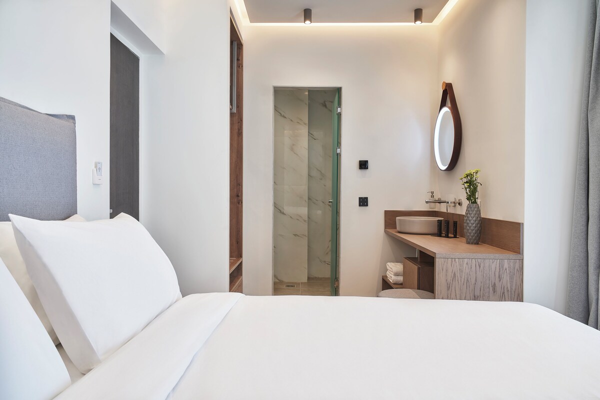 Habitació d'hotel moderna amb llit, bany amb dutxa i tocador amb mirall.