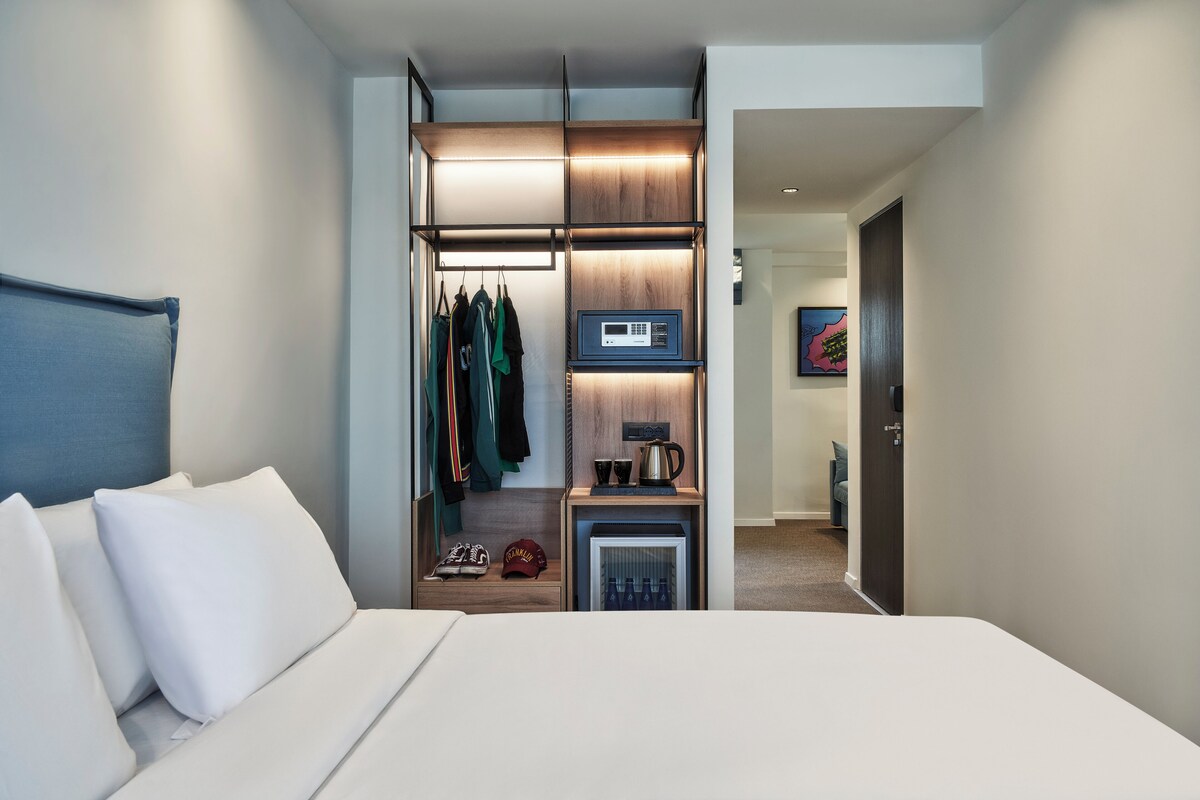 Habitació d'hotel amb llit, armari ple de roba penjada, microones i nevera petita.