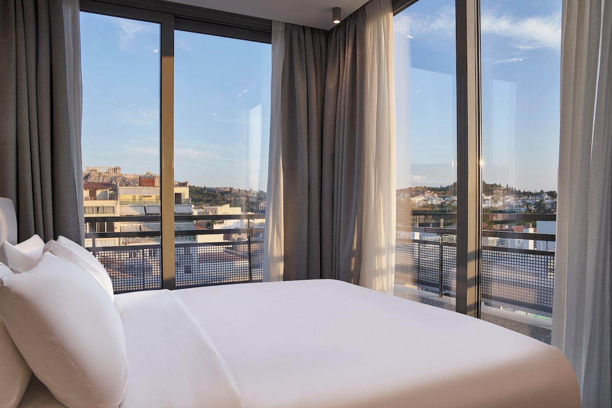 Habitació d'hotel amb un llit gran, vista a la ciutat i un balcó amb barana.