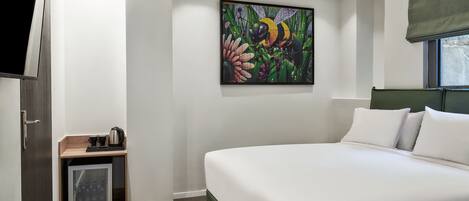 A bedroom with a large bed, a painting of a bee on the wall, a small cabinet with a kettle, and a window with a view.
