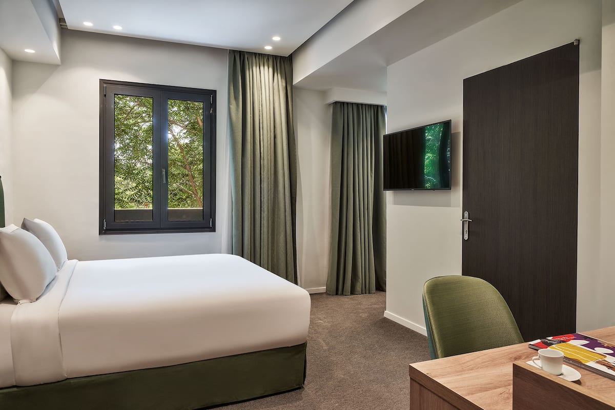 Camera d'albergo con un letto, una scrivania, una sedia, una TV e una finestra con tende.