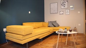 Un salon moderne avec un canapé jaune, une petite table sur laquelle repose un magazine et des œuvres d’art murales.