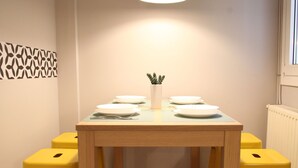 Un coin repas avec une table en bois, deux tabourets jaunes et une suspension.
