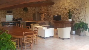 A spacious kitchen with a stone wall, wooden ceiling, and a dining area with a wooden table and chairs. - Gîte Domaine de La Gravette (Cubnezais)